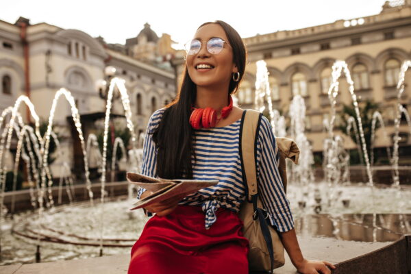 cool-brunette-woman-striped-shirt-red-skirt-headphones-eyeglasses-smiles-sits-near-fountain-holds-map (1) Study in Italy Made Simple